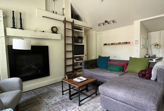 Living room with grey sectional and decorative cushions, in front of a fire place and library ladder on the wall
