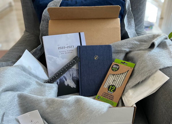 Subscription box with planner, journal, colouring pencils, ruler and alpaca scarf on a grey chair