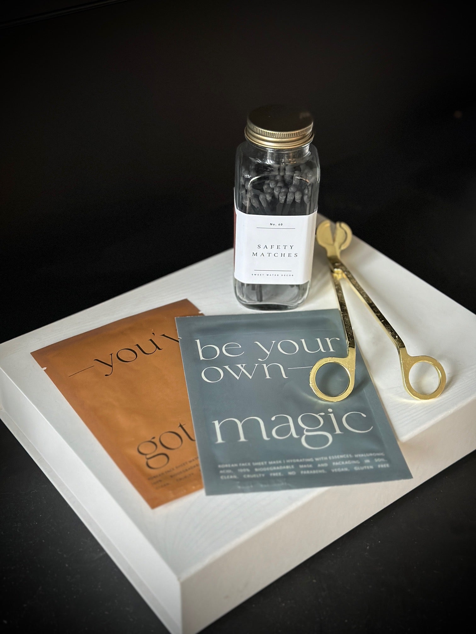 jar of safety matches, gold candle wick trimmer and facial sheet masks displayed on a white box