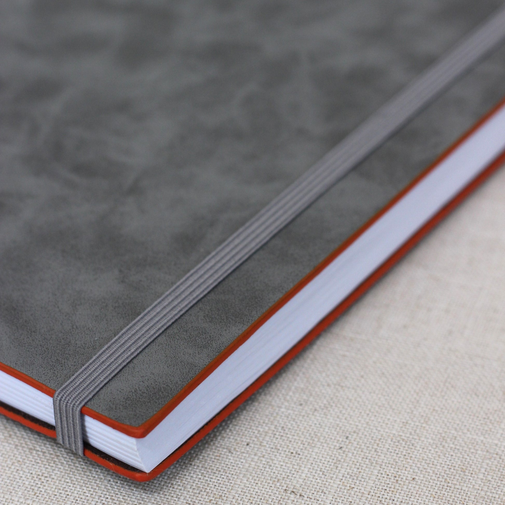 Close up angled view of grey faux vegan leather journal's oiled edge, grey elastic band and white recycled paper