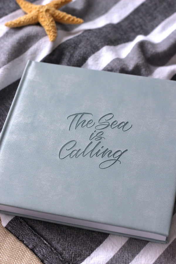 The Sea is Calling square journal on a grey and white striped beach towel